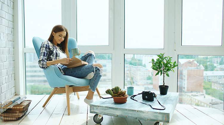 A woman reclines in a blue chair while reading.